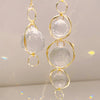 Un couple de pendentifs en cristal doré avec des pierres claires et arrondies, suspendus sur un fond blanc.