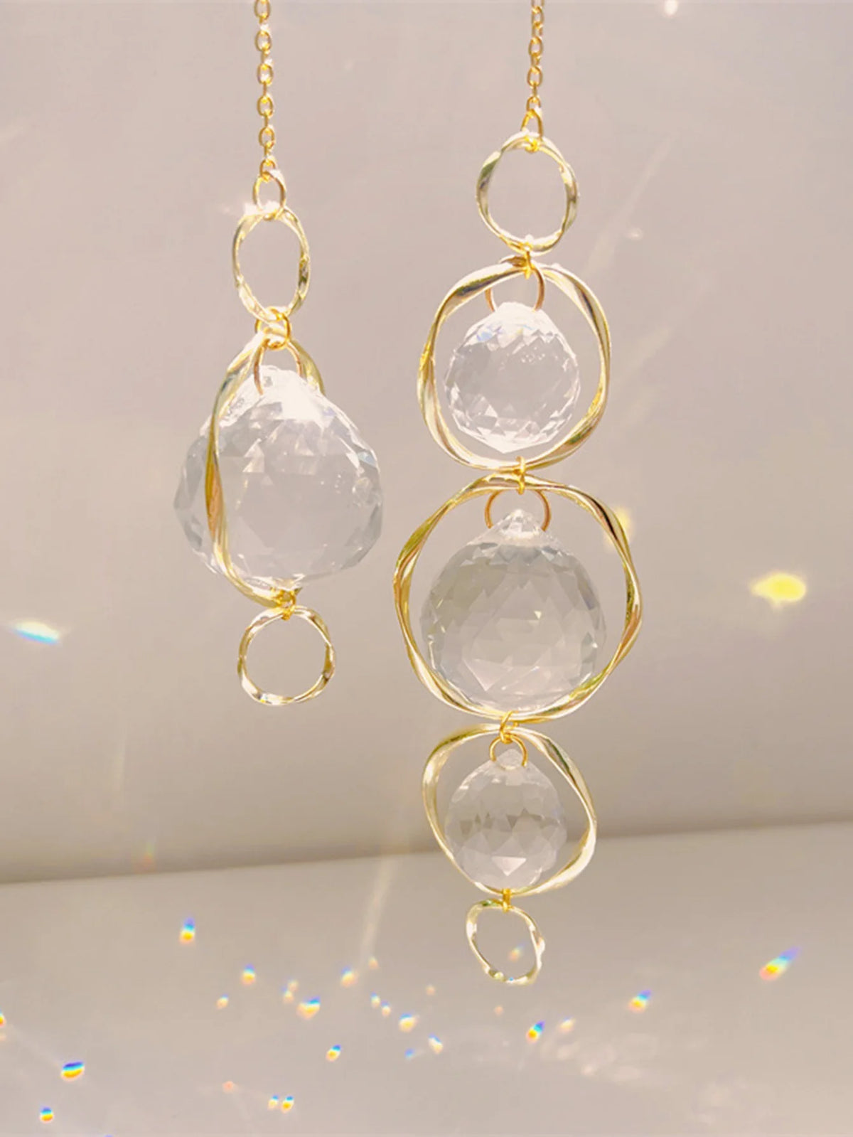 Un couple de pendentifs en cristal doré avec des pierres claires et arrondies, suspendus sur un fond blanc.