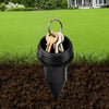 A black garden key hider with a loop holding several brass keys is partially buried in dark soil.
