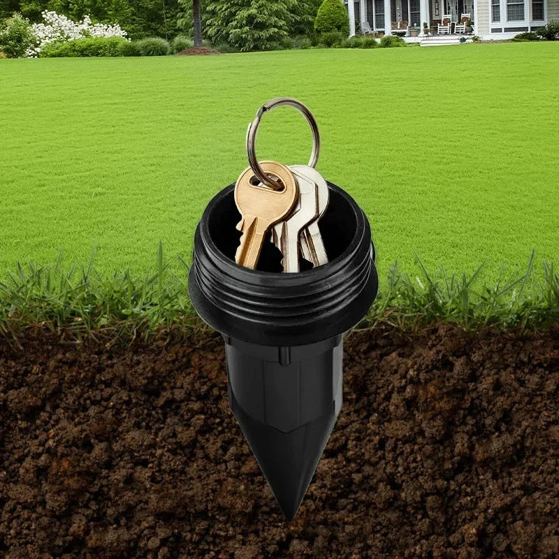A black garden key hider with a loop holding several brass keys is partially buried in dark soil.