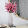 A bouquet of pink cherry blossom and gypsophila artificial flowers in a tall, translucent vase on a white surface.