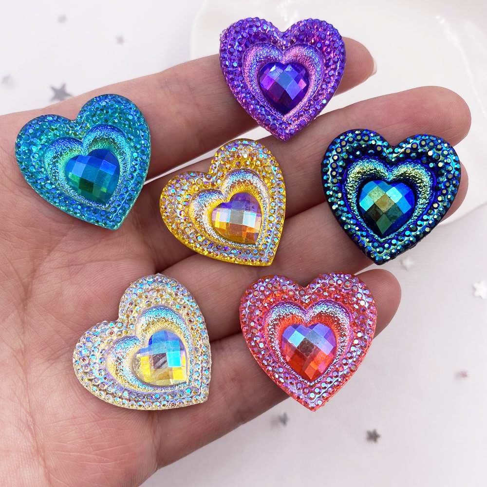 A hand holds a set of twelve heart-shaped iridescent and colorful resin rhinestone flatbacks.