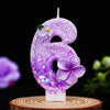 A purple glitter flower number candle shaped like the number 6 displayed on a wooden surface.