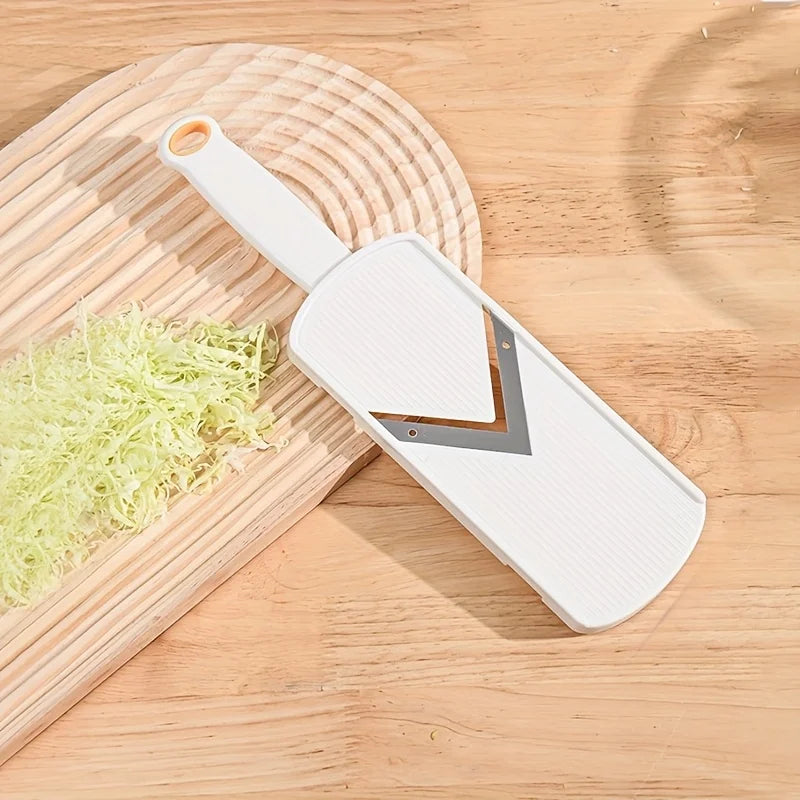 A white manual cabbage shredder with stainless steel blades resting on a wooden cutting board.