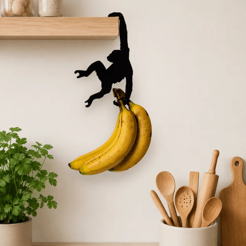 A black monkey-shaped storage hook is hanging on a shelf, positioned above a bunch of yellow bananas.