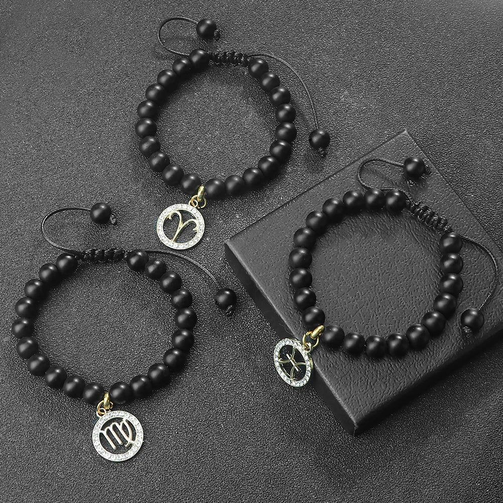 Black beaded zodiac bracelets and necklaces with gold accents displayed on a dark surface.