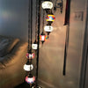 A hanging light fixture with multiple colorful glass bulbs and a dark metal chain, mounted on a wall.