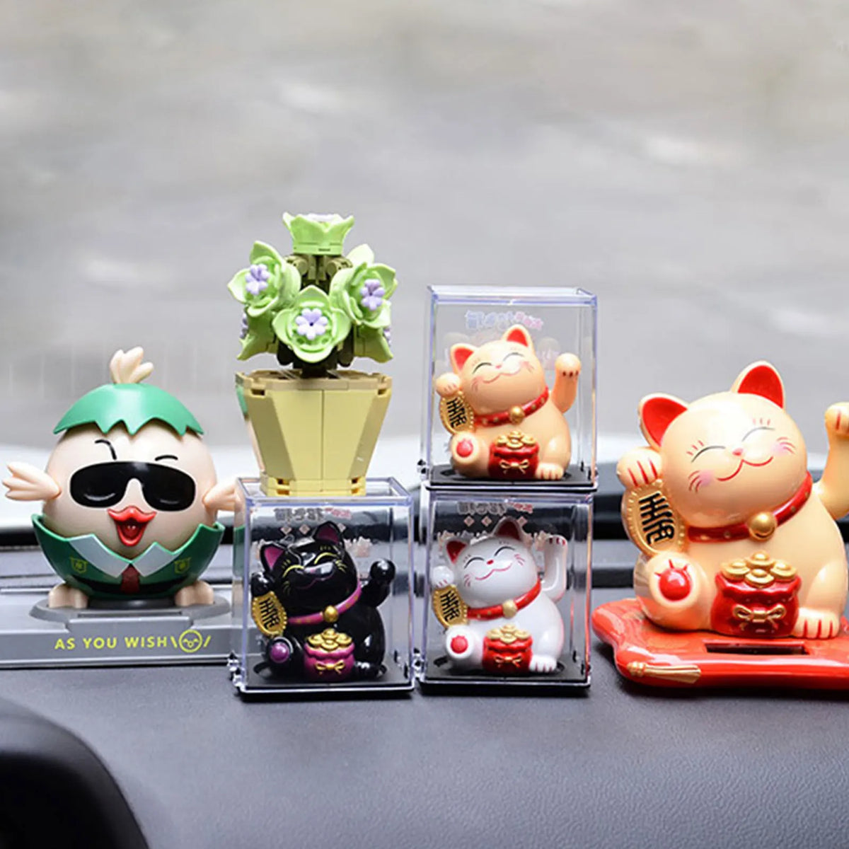 A collection of solar-powered waving lucky cat figurines in various colors and designs displayed on a dark surface.