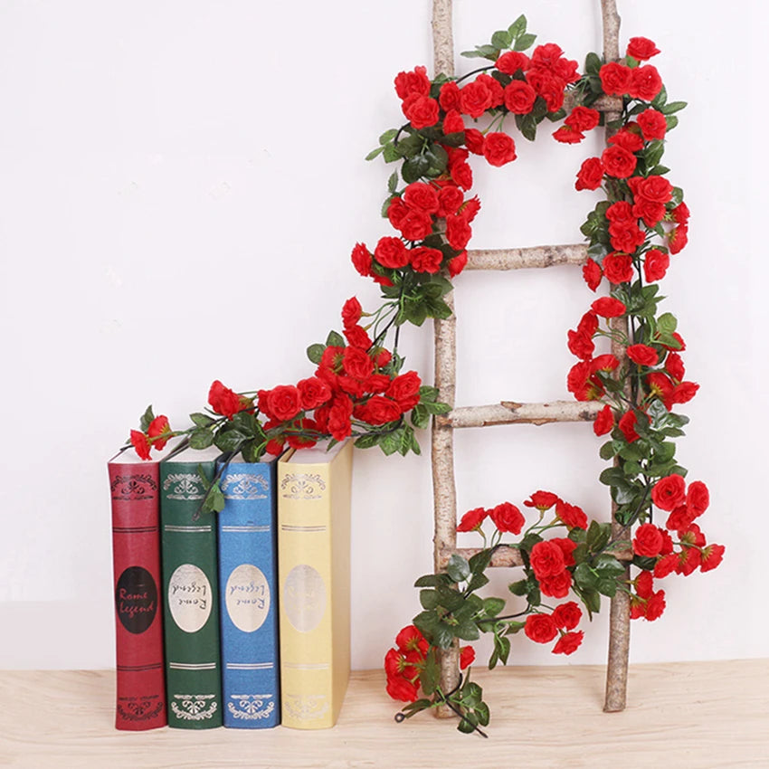 A silk rose vine garland is displayed on a wooden ladder next to books for wedding and home decor.