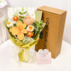 A bouquet of handmade crochet tulips in orange and cream flowers wrapped in green paper and presented in a brown box.