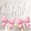 A white balloon banner spelling out Happy Birthday with pink accents, displayed above a wooden table.