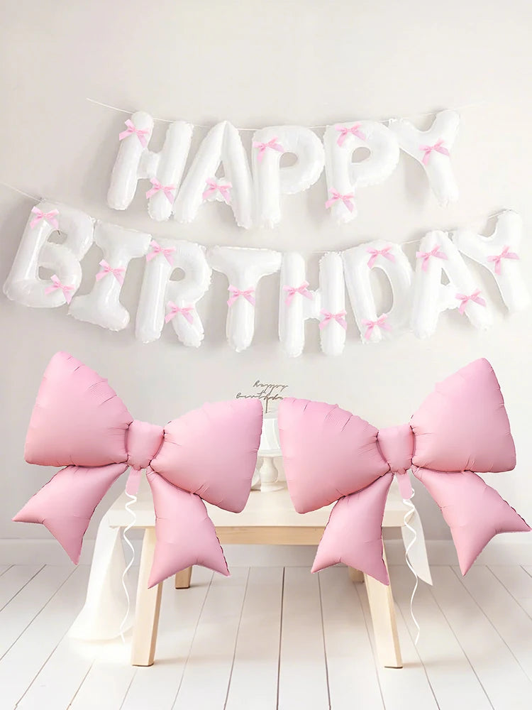 A white balloon banner spelling out Happy Birthday with pink accents, displayed above a wooden table.