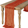 A rust orange semi-sheer gauze table runner draped over a wooden table.