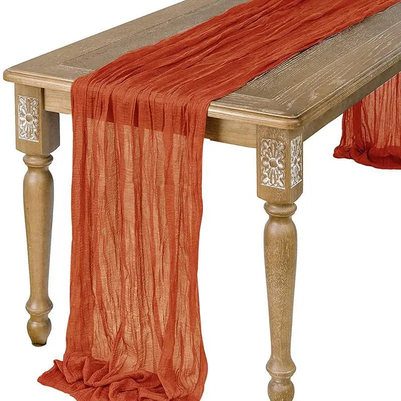 A rust orange semi-sheer gauze table runner draped over a wooden table.