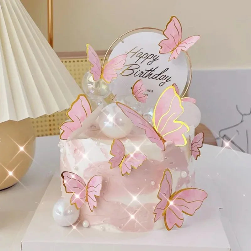 A pink and white layered cake decorated with gold butterfly toppers on a white platter.