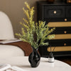 A black ceramic vase with an abstract grass motif holding green foliage on a white table.