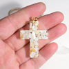A clear resin cross charm with white and yellow flecks is held in a hand.