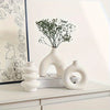 A white ceramic vase set featuring a textured, organic shape and a sprig of green foliage on a white shelf.