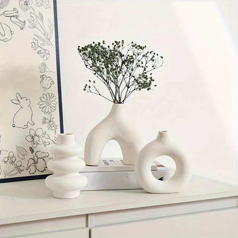 A white ceramic vase set featuring a textured, organic shape and a sprig of green foliage on a white shelf.