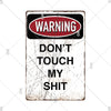 A vintage metal warning sign with a red oval banner that reads WARNING and black text below that says DON'T TOUCH MY SHIT