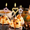 A collection of birthday candles featuring pink, gold, and silver star and heart shapes placed on muffins.