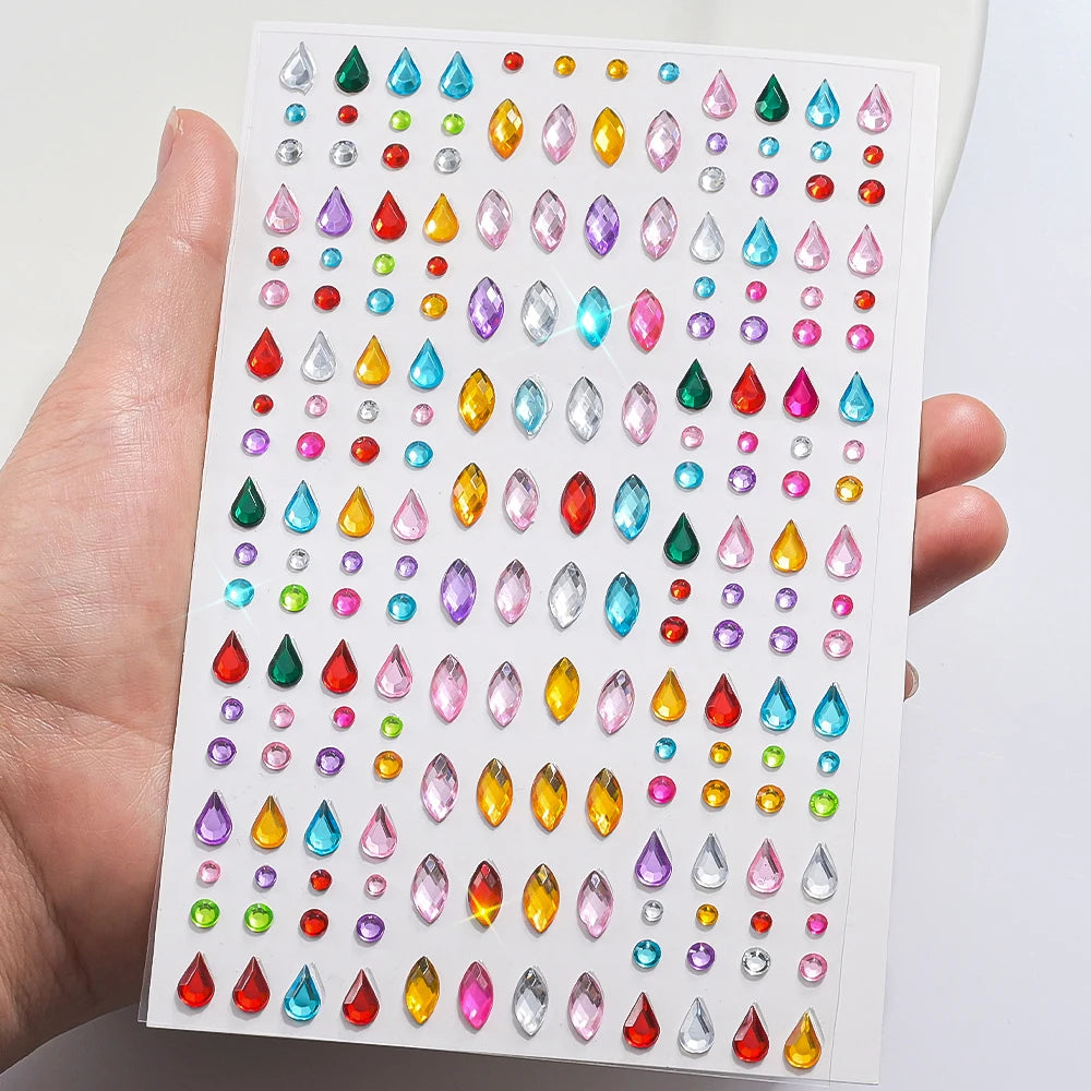 A hand holds a sheet of glitter gem stick-on facial tattoos featuring various colored gemstones.