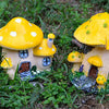 A yellow resin mushroom house garden statue with a large cap and small windows nestled in green grass.