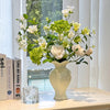 Elegant ceramic vase with white flowers and green foliage displayed on a light surface.