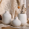 A set of three minimalist white ceramic decorative vases displayed on a textured fabric.