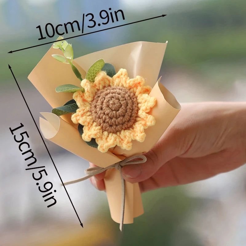 A hand holds a bouquet of handmade crochet flowers, featuring a large yellow and brown sunflower, with dimensions marked.