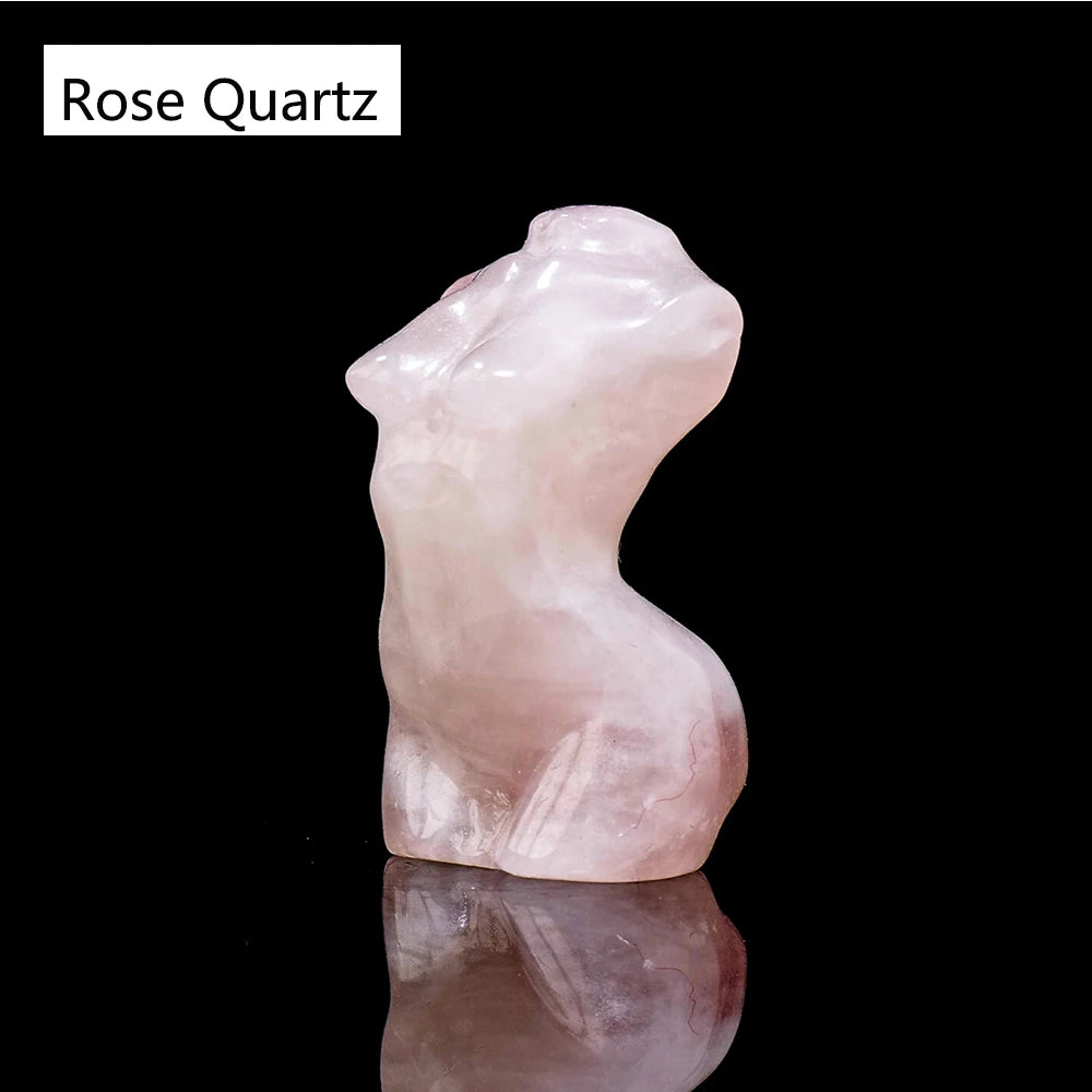 Una figura de cuarzo rosa translúcido y suave con forma de torso femenino, reflejándose en una superficie oscura.