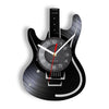 A black electric guitar shaped wall clock with a vinyl record face and hands.