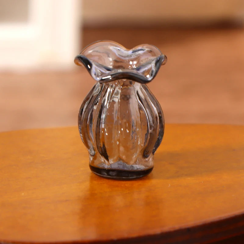 A clear glass miniature dollhouse vase and wine bottle set sitting on a wooden surface.
