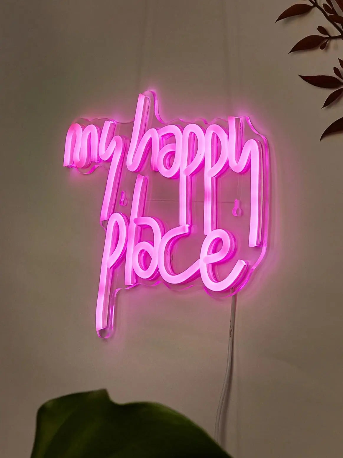 Pink neon sign spelling out My Happy Place mounted on a white wall.