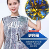 A young woman wearing a sports jersey is holding a bright blue and yellow pom pom in her hand.