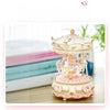 A delicate pink and gold handmade resin carousel music box with ornate detailing on a wooden surface.