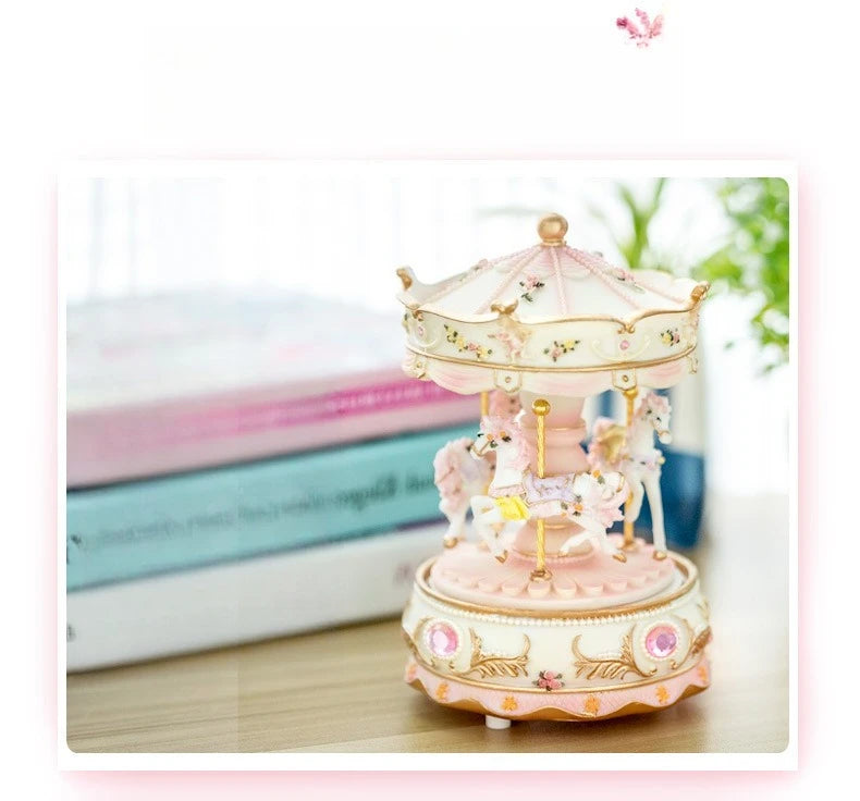 A delicate pink and gold handmade resin carousel music box with ornate detailing on a wooden surface.