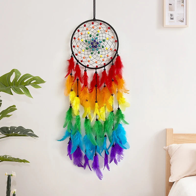 A colorful feather dream catcher pendant with vibrant yellow, green, and purple feathers hanging on a white wall.