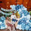 Una mujer sentada rodeada por un gran guirnalda de globos azules y plateados en un evento al aire libre.