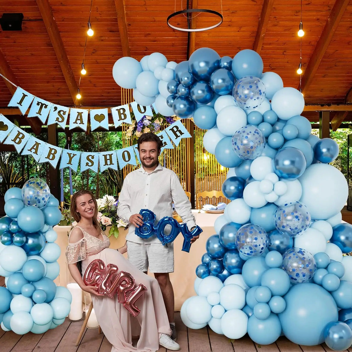 Una mujer sentada rodeada por un gran guirnalda de globos azules y plateados en un evento al aire libre.