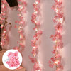 Pink cherry blossom string lights garland draped vertically on a white wall.