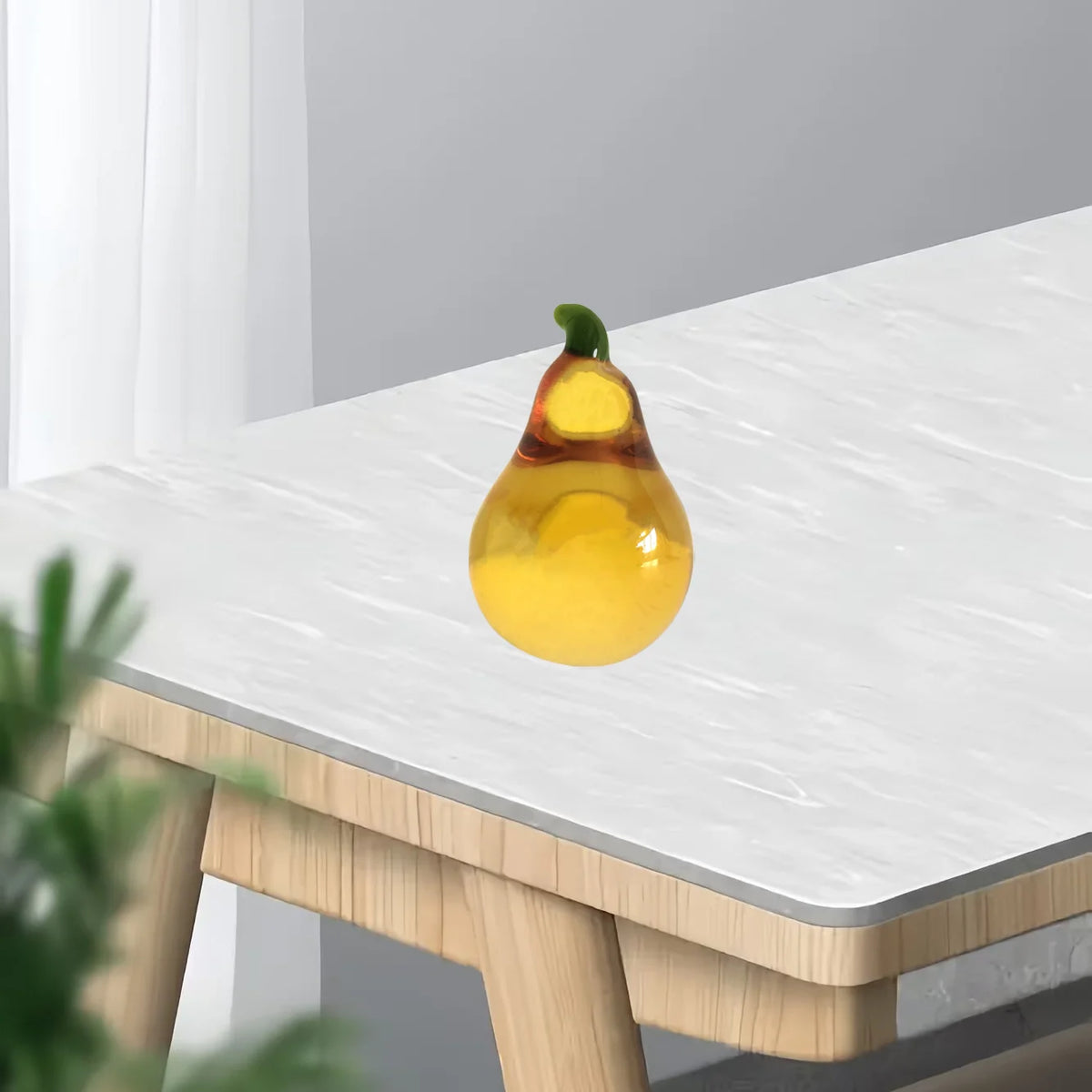 A yellow crystal glass pear figurine used as a home decor accent on a white table.