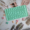 A silicone mold set with alphabet letters and numbers in a mint green color is shown on a white surface.