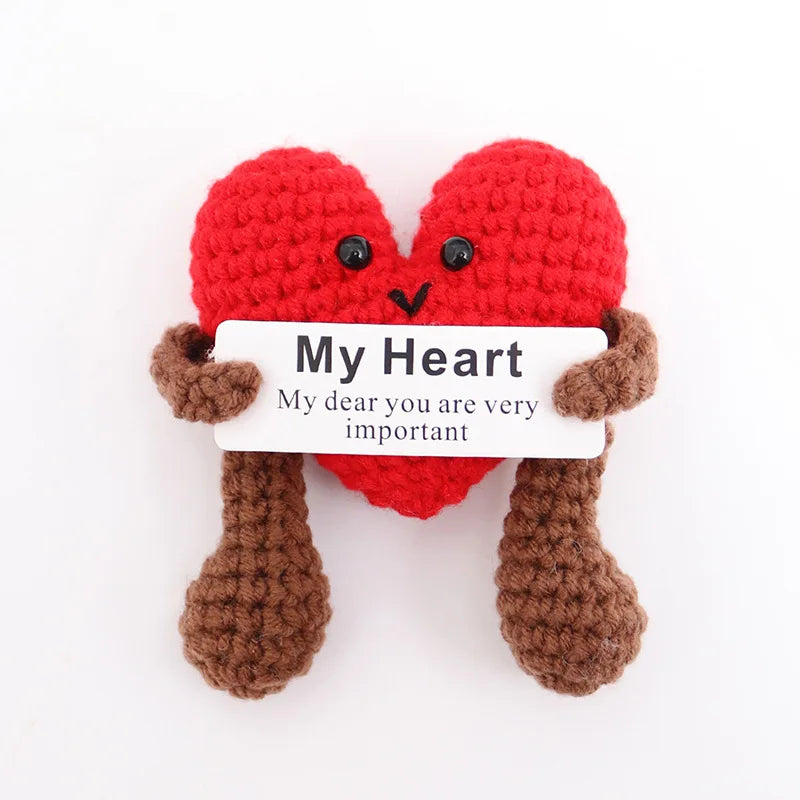 A handmade red knitted plush doll shaped like a heart with brown knitted legs and a white tag reading My Heart