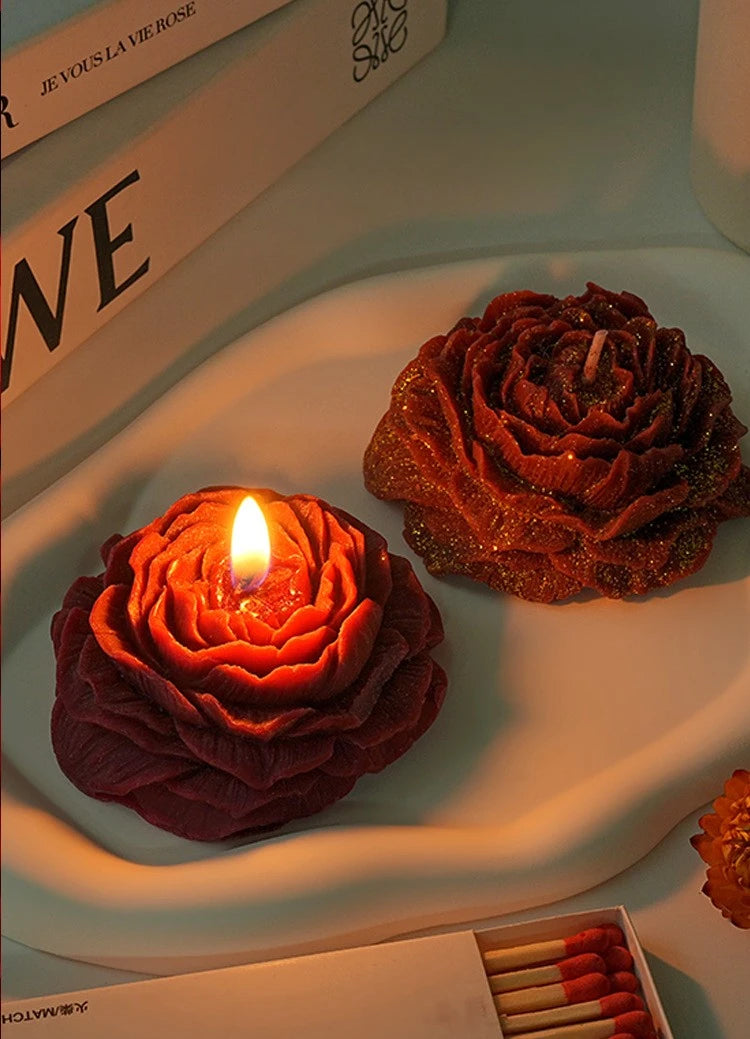 Nahaufnahme einer tiefroten handgemachten Rosen-Päon-Duft-Sojawachs-Kerze auf einer weißen Platte neben einem Buch.