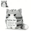 A handmade crochet mini cat plush toy in gray and white yarn with a tag that reads Positive Cat