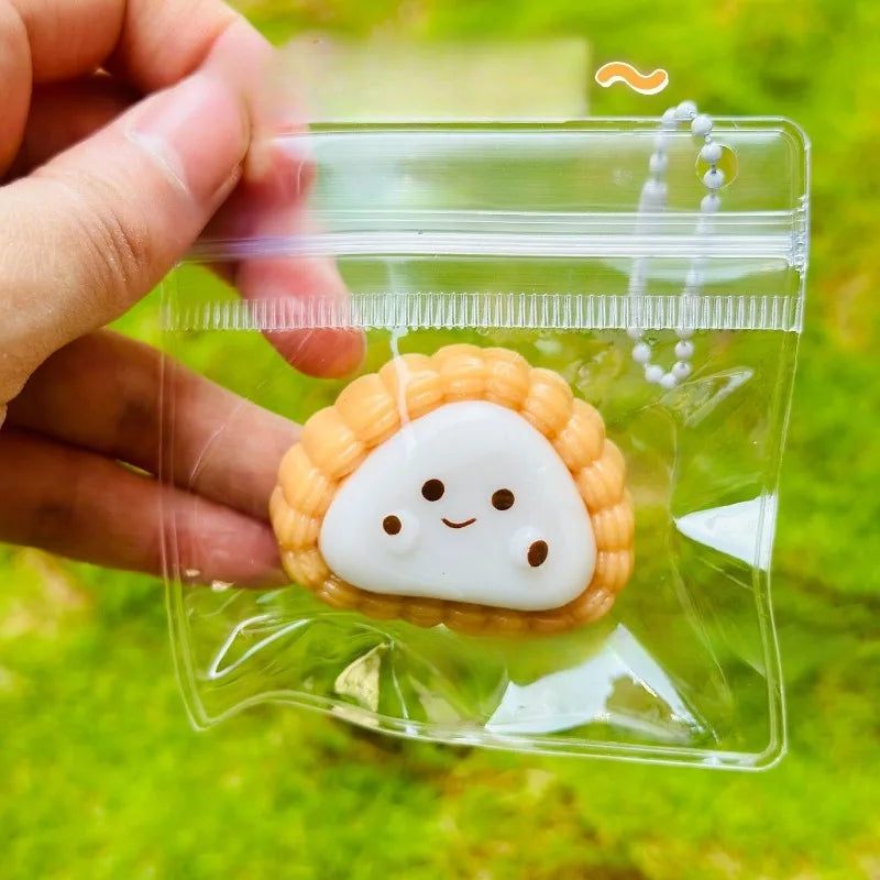 A small white cartoon food squeeze toy keychain shaped like a smiling avocado is held in a clear plastic pouch.