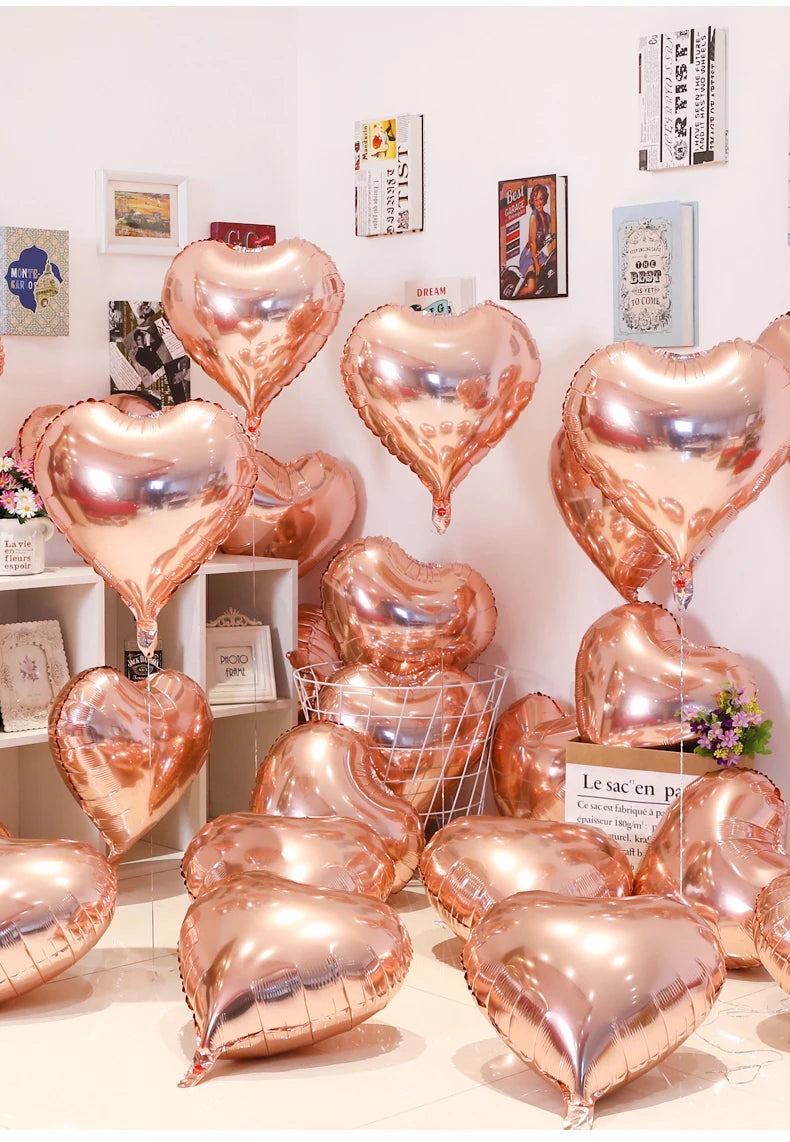 A collection of rose gold heart foil balloons displayed on a white surface.