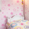 A pink star vinyl wall decal featuring various sized stars on a wall, next to a white bed frame.