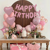 A pink marble birthday balloon decoration set featuring a wooden banner, balloons, and floral accents.